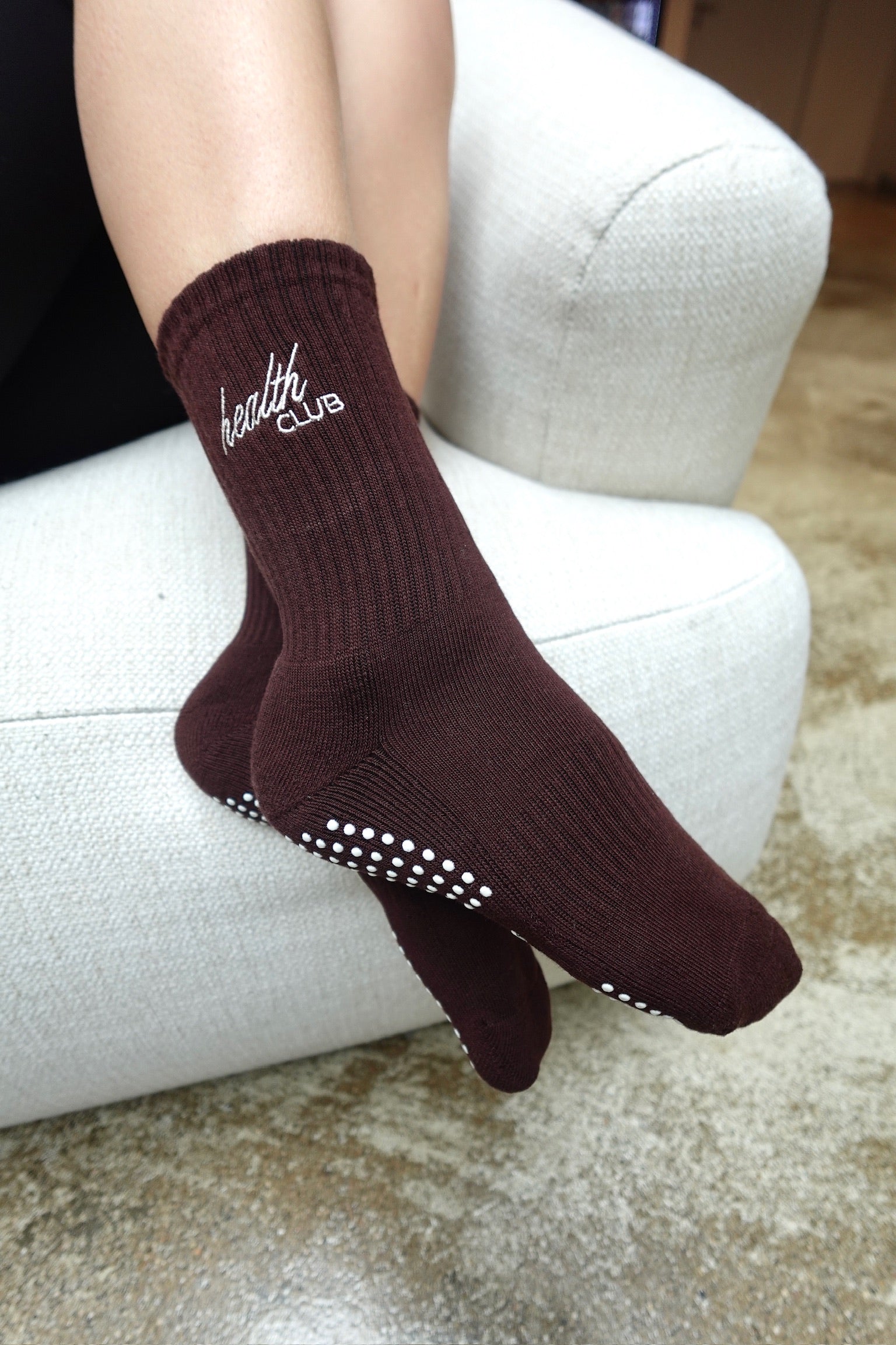 Pilates-Socken in der Farbe Espresso, „Health Club“ mit weißen Anti-Rutsch-Noppen, getragen auf hellem Sessel