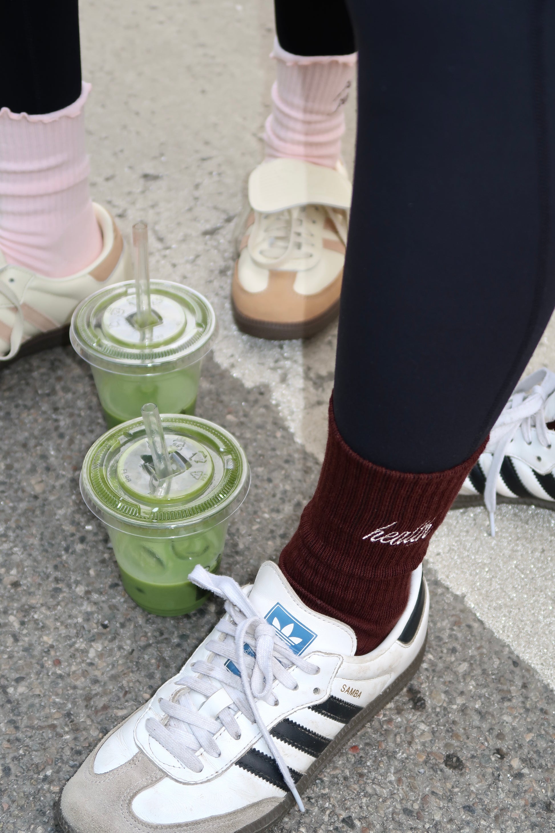 Braune „Health Club“-Socken und rosa „Pilates Princess“-Socken mit weißen Retro-Sneakern und zwei Matcha-Drinks
