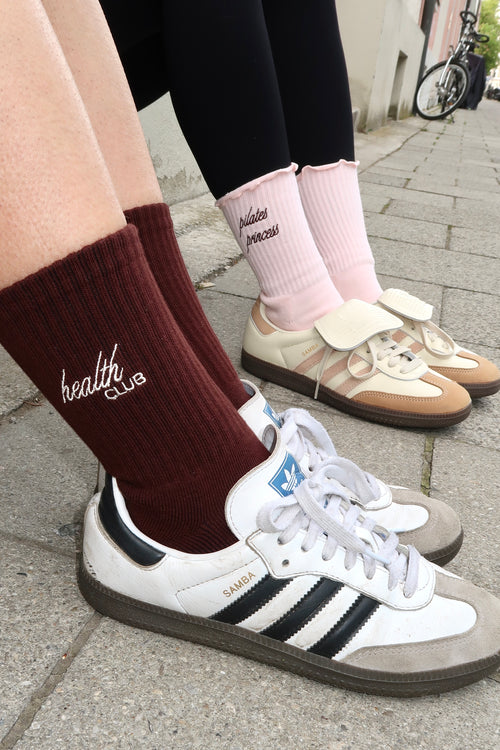 Braune „Health Club“-Socken und rosa „Pilates Princess“-Socken, kombiniert mit Retro-Sneakern, Straßenaufnahme